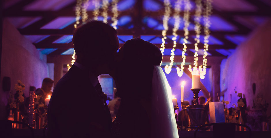 Couple silhouetted kissing infront of wedding party at night
